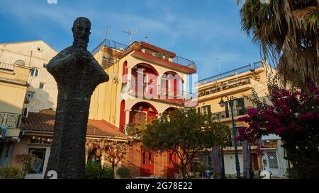 Zakynthos, ville de Zakynthos, centre-ville, bâtiments, lumière du matin, Statue du moine Anthimos Argyropoulos, à l'ombre, derrière lui bâtiments dans la lumière du matin, ciel bleu avec des nuages plus sages Banque D'Images