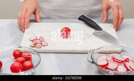 Radis frais tranchés gros plan sur une planche à découper en marbre sur fond gris clair. Préparation de salades de légumes, recette Banque D'Images