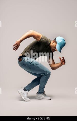 Danseur latin non reconnu portant un chapeau amusant en studio tourné sur fond blanc faisant des mouvements de hip hop. Banque D'Images