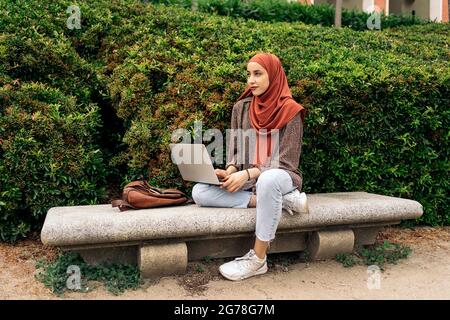 Jeune femme musulmane portant le hijab assise dans le parc et utilisant son ordinateur. Banque D'Images