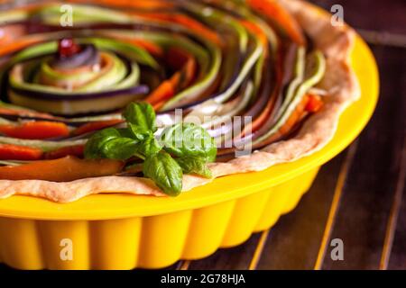 Le processus de cuisson d'une tarte en spirale de légumes avec des courgettes, aubergines, carottes avec basilic dans un plat de cuisson en silicone, macro gros plan Banque D'Images