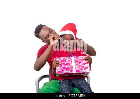 Drôle de famille souriante ont du plaisir, le père et le fils avec chapeau de noël sur la tête tiennent un cadeau à la main. Le père arrange le chapeau de son fils. Banque D'Images