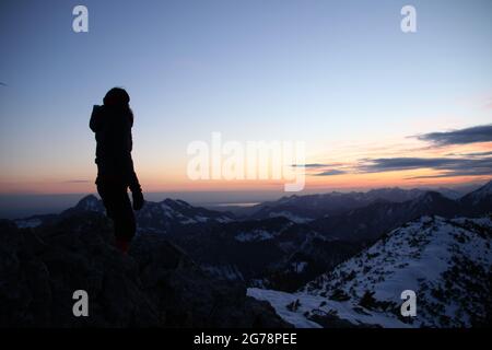 La jeune femme bénéficie du lever du soleil et de la vue de l'Auerspitz (1811m) vers Chiemgau, Wendelstein (1873m) laissé derrière la femme et Großer Troithen (1851m) à l'extrême droite, atmosphérique, haute-Bavière, Bavière, Allemagne,Alpes bavaroises, montagnes de Mangfall Banque D'Images