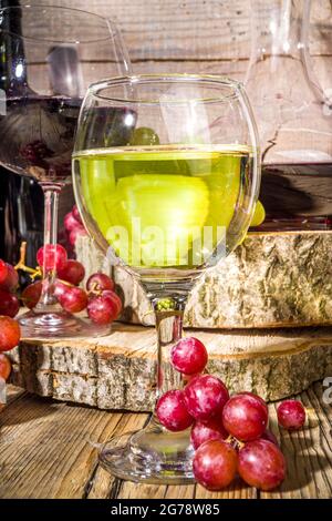 Verres de vin rouge et blanc avec soleil et ombres, avec bouteille et décanter, bouquet de raisins, sur fond de bois avec tourteaux biologiques, autum Banque D'Images