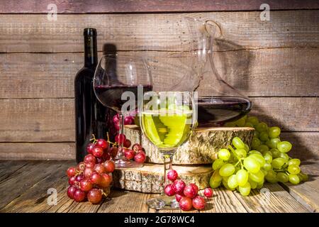 Verres de vin rouge et blanc avec soleil et ombres, avec bouteille et décanter, bouquet de raisins, sur fond de bois avec tourteaux biologiques, autum Banque D'Images