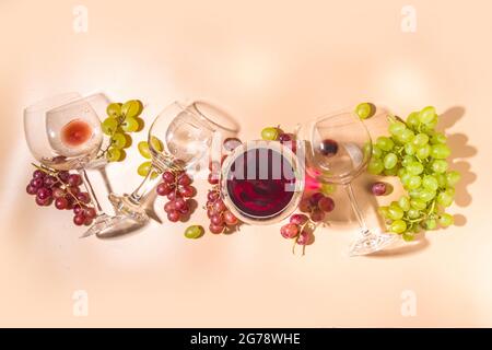 Verres de vin rouge et blanc avec soleil et ombres, avec bouteille et carafe, bouquet de raisins, sur fond crémeux, vue sur le dessus plat vin Banque D'Images