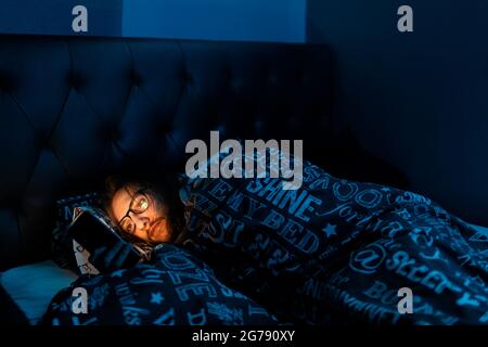 Un jeune homme accro aux médias sociaux vérifiant son téléphone avant d'aller au lit, toxicomanie, médias sociaux, après sombre concept Banque D'Images