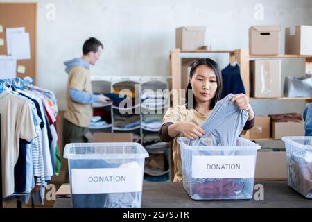 Jeune femme asiatique choisissant des vêtements dans des boîtes de dons Banque D'Images