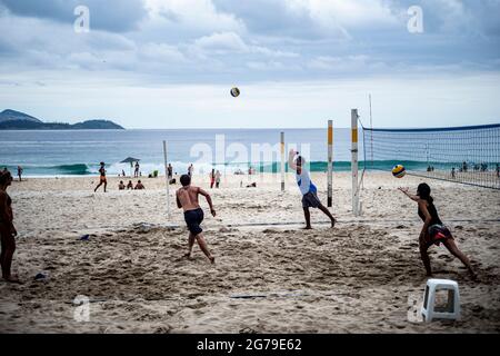 Un groupe de jeunes Brésiliens jouent au volley-ball au coucher du soleil à l'extrémité Leme de la plage de Copacabana. Banque D'Images