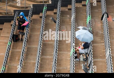 Hambourg, Allemagne. 12 juillet 2021. Tennis: ATP Tour - Hambourg, célibataires, hommes, 1er tour au Stadion am Rothenbaum. Moutet (France) - Baez (Argentine). Les spectateurs s'assoient avec des parasols sous la pluie protégés sur la Tribune. Credit: Daniel Bockwoldt/dpa/Daniel Bockwoldt/dpa/Alay Live News Banque D'Images