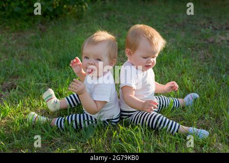 Les filles jumelles sont assises sur l'herbe verte avec leur dos l'une à l'autre. Banque D'Images