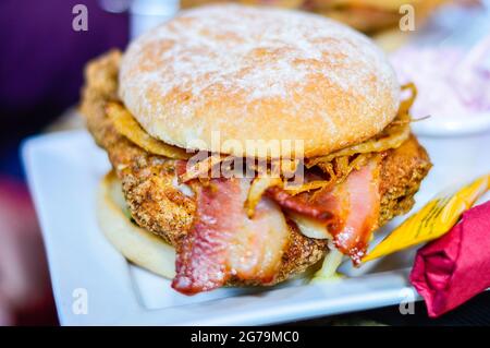 Gros plan du hamburger avec poulet, bacon et oignons frits sur la plaque blanche Banque D'Images