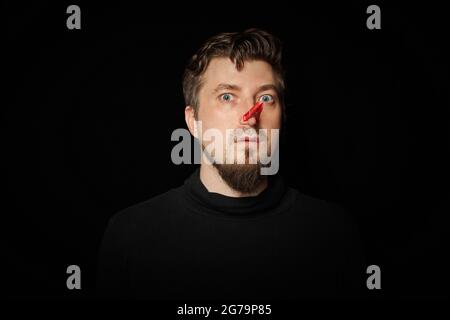 Homme barbu avec une épingle à linge sur le nez. Mauvaise piqûre, drôle de prankster, concept de plaisanterie. Rire de vous-même. Épinglette rouge - symbole de la moquerie et de la plaisanterie Banque D'Images