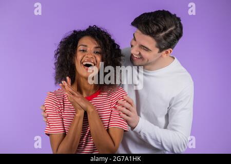 Homme blanc avec sa chère amie afro-américaine après la surprise. Couple interracial sur fond de studio violet. Amour, vacances, bonheur Banque D'Images