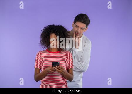 Beau homme est peeking sur l'épaule des amies africaines, elle communique par téléphone mobile.Guy choqué par la jalousie et la trahison de la femme Banque D'Images