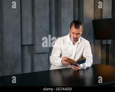 Un homme dans la chambre sombre et moderne lit un vieux livre. Banque D'Images