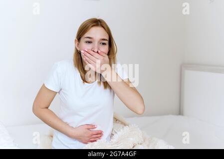 La jeune femme se sent nauséabonde sur le lit. Vomissez bientôt. Empoisonnement, problèmes d'estomac. Banque D'Images