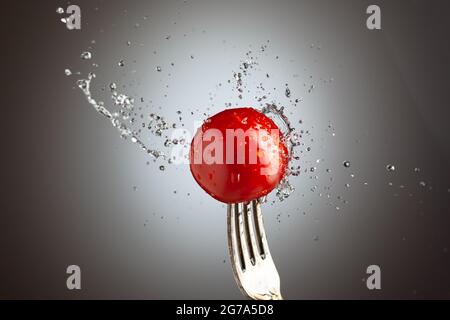 cerise de tomate sur une fourchette dans des éclaboussures d'eau. Arrière-plan noir et blanc Banque D'Images