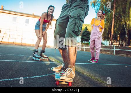 Un jeune garçon sur le skate avec deux filles derrière lui acclamations et rire Banque D'Images