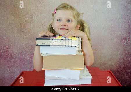 bel enfant blond avec de grands yeux bleus et des cheveux blonds avec pile de livres Banque D'Images