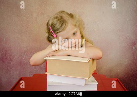 fille aux cheveux blonds cachés derrière une pile de livres Banque D'Images