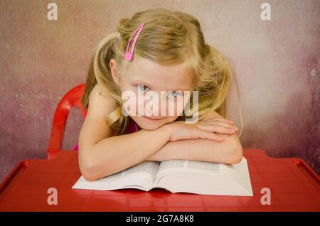 belle fille blonde avec de grands yeux bleus et des cheveux blonds avec pile de livres Banque D'Images