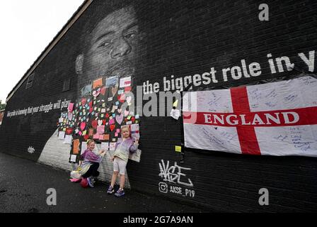 Ruby Swave, 7 ans (à gauche) et sa sœur Reeva Swave, 4 ans, placent des messages de soutien au-dessus des sacs poubelle qui ont été placés sur des mots offensifs sur la fresque de l'attaquant de Manchester United et du joueur d'Angleterre Marcus Rashford sur le mur du café Coffee House sur Copson Street, Withington, Qui semblait vandalisé le matin après que l'équipe de football d'Angleterre a perdu la finale de l'UEFA Euro 2021. Date de la photo: Lundi 12 juillet 2021. Banque D'Images