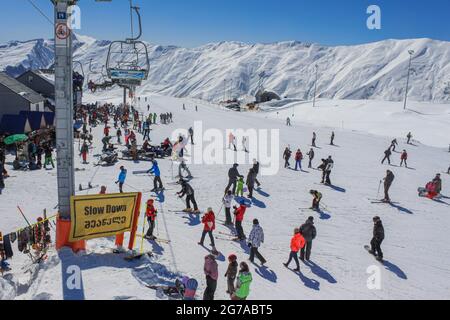 Géorgie, Gudauri, 8 mars 2013 : téléphérique, skieurs et snowboardeurs sur la piste de la station de ski. Sur fond de sommets enneigés et de bl Banque D'Images