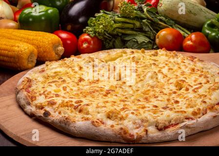 Pizza au poulet et à la mozzarella sur une planche de bois et légumes en arrière-plan. Banque D'Images