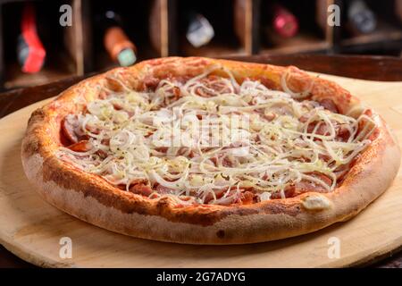 Pizza à la saucisse de pepperoni avec oignon sur une planche de bois. Pizza brésilienne. Banque D'Images