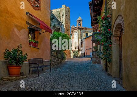 L'étroite rue pavée parmi les maisons colorées mène à la petite église sous le ciel bleu dans la vieille ville de Monforte d'Alba dans le Piémont, le nord de l'Italie. Banque D'Images