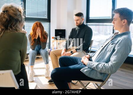 Vue de face d'une jeune femme triste et frustrée partageant un problème pendant une thérapie de groupe assise avec la tête badurée. Banque D'Images