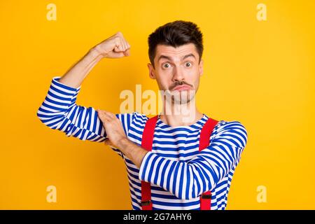 Photo de jeune funky choqué surpris homme surpris marin montrant biceps isolés sur fond jaune Banque D'Images