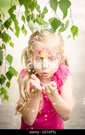 petite jolie fille blonde avec le visage coloré soufflant Banque D'Images