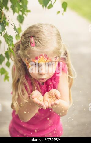 petite jolie fille blonde avec le visage coloré soufflant Banque D'Images