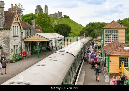 Château de Corfe, Dorset, Angleterre - juin 2021 : personnes se trouvant sur un train à vapeur d'époque à la gare de Corfe Castle. Le château est en arrière-plan. Banque D'Images