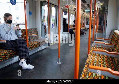 Jeune femme avec téléphone mobile assis portant un masque de visage covid sur Lea Valley ligne Overground train intérieur Londres Angleterre Royaume-Uni Banque D'Images