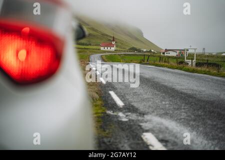 La voiture s'est arrêtée sur la route avec vue sur l'église islandaise rurale typique avec un toit rouge dans la région de Vik. Islande Banque D'Images