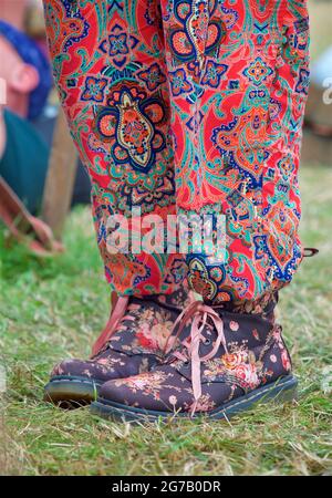 Une jeune femme porte un pantalon coloré et des bottes Dr Marten à motif fleuri. Festival Womad, Angleterre Banque D'Images