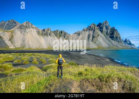 Homme randonneur avec sac à dos sur les dunes de sable noir sur la pointe de Stokksnes sur la côte islandais du sud-est avec Vestahorn. Matin d'été coloré Islande, Europe. Banque D'Images