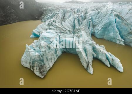 Vue aérienne en haut du mur de langue bleu glacier et lagune d'eau glaciaire boueuse à Fjallsarlon, Islande Banque D'Images