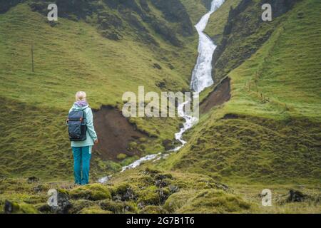 Femme touriste avec sac à dos en face de la cascade islandaise de montagne près de Fjadrargljufur sur la côte sud de l'Islande Banque D'Images