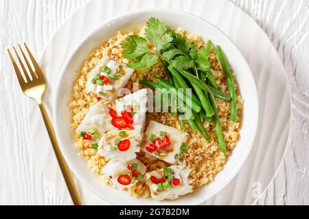 Bacalhau com todos, morue au bulgur, haricots verts cuits à la vapeur, saupoudrée de piments forts et d'oignons verts dans un bol blanc sur une table en bois, balkans Banque D'Images