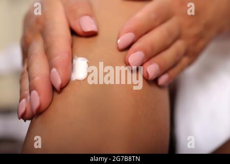 Les mains de femmes appliquant de la crème blanche sur sa jambe à la maison. La fille porte une serviette blanche. Soin de la peau et concept de beauté Banque D'Images