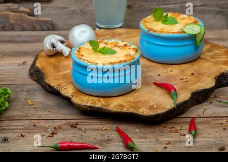 Pots avec julienne de champignons sur une planche en bois, décorés avec des herbes. Julienne à la cocotte à la croûte de fromage jaune. Banque D'Images