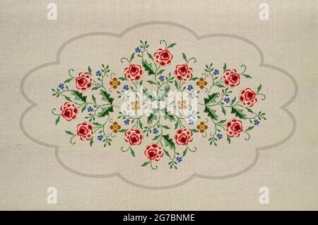 Motif pour la broderie d'un ornement de brindilles avec des fleurs de roses rouges-roses avec des feuilles, des coquelicots et des fleurs bleues dans un cadre ovale ondulé gris contre un Banque D'Images