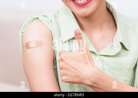 Jeune femme asiatique montrant le pouce gestante vers le haut ou comme et son bras avec bande de plâtre aide après le coronavirus Covid-19 injection sur l'épaule, coron Banque D'Images