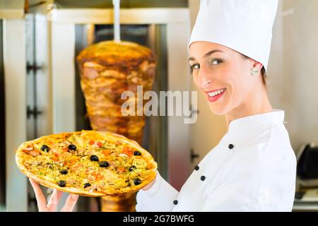 Döner Kebab - friendly female vendeur dans un restaurant fast food turc, tenant une pizza en face de brochette Banque D'Images