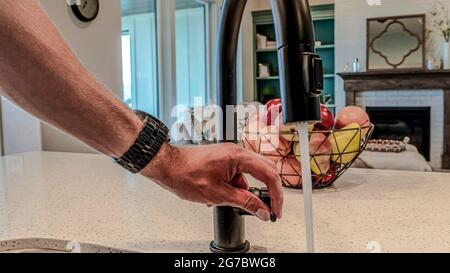 Pano main mâle sur le levier du robinet avec l'eau fron le bec noir à l'intérieur de la cuisine Banque D'Images