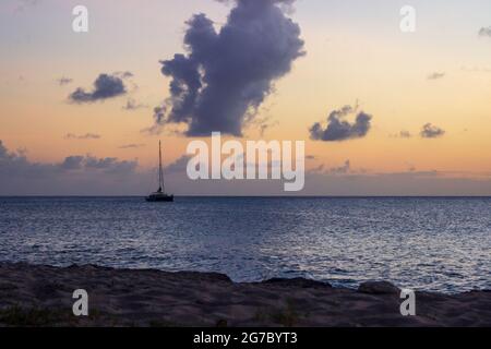 Un voilier amarré dans les Caraïbes au large de la rive près de Frederiksted, Sainte Croix, USVI comme le coucher du soleil se reflète dans les nuages et la mer. Banque D'Images